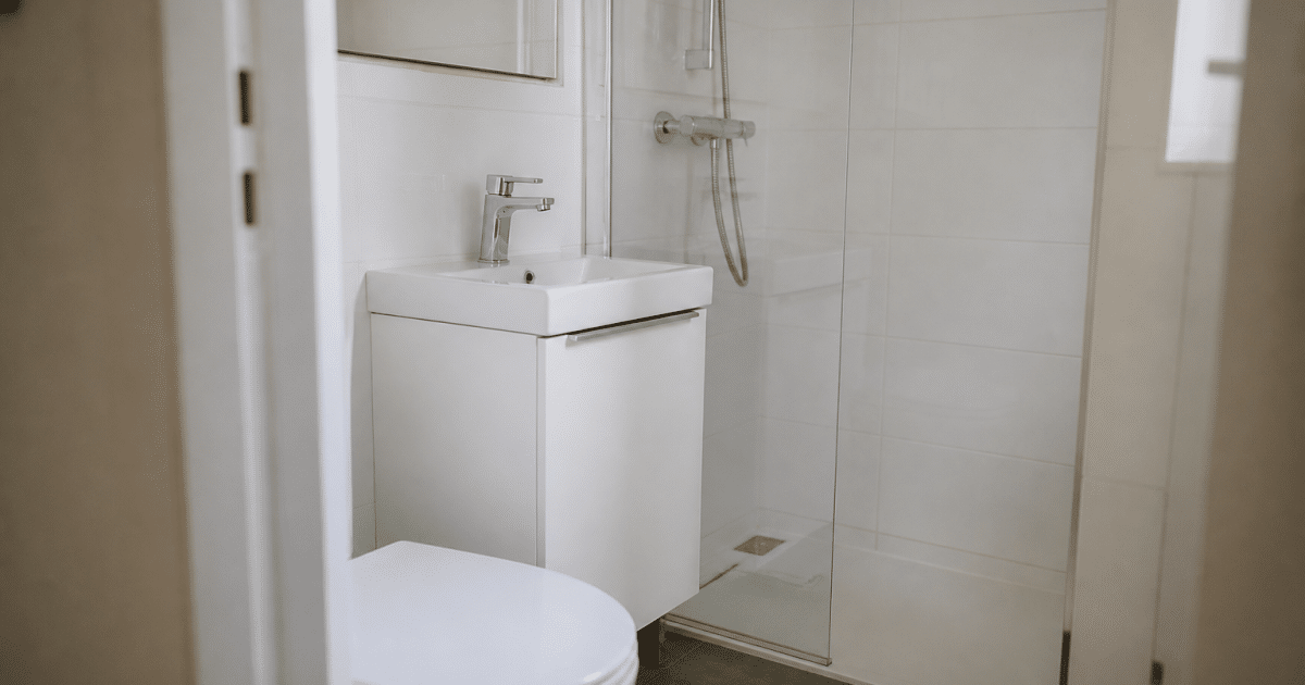 Petite salle de bain blanche avec toilettes, lavabo compact et douche intégrée