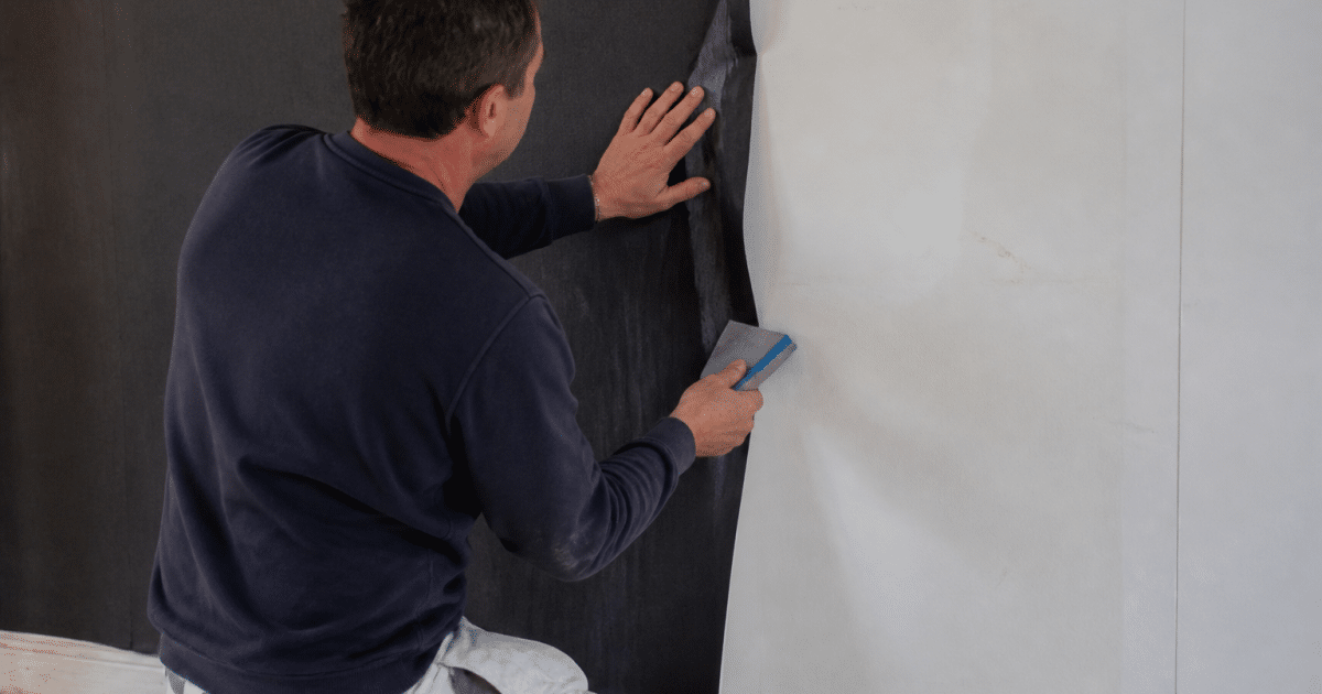 ouvrier appliquant papier peint noir sur mur blanc avec spatule