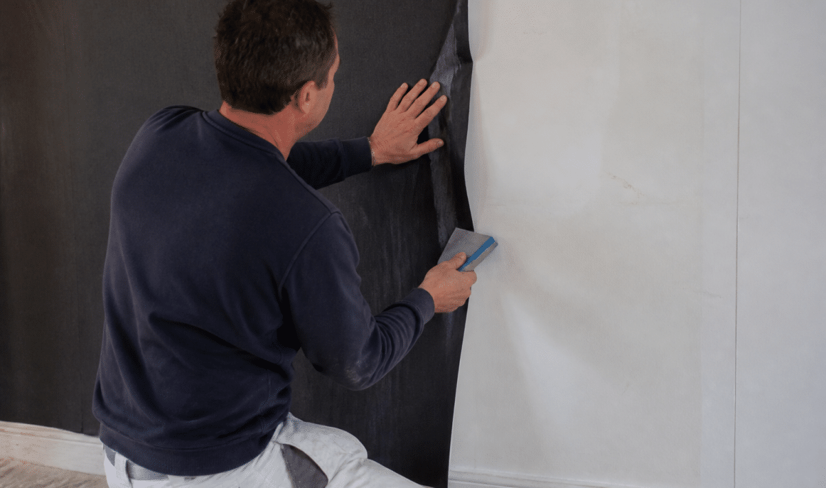 ouvrier appliquant papier peint noir sur mur blanc avec spatule
