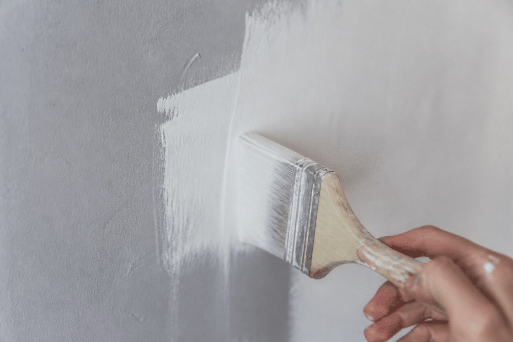 Pinceau appliquant primaire blanc sur mur mat gris clair