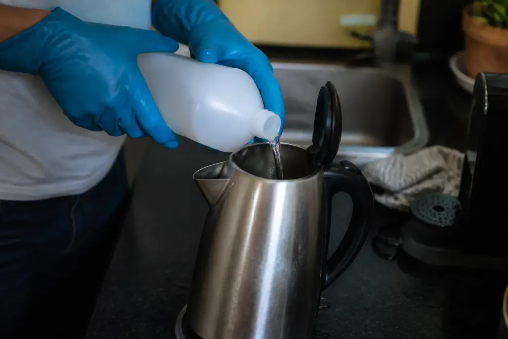 Mains gantees versant du detartrant dans une bouilloire
