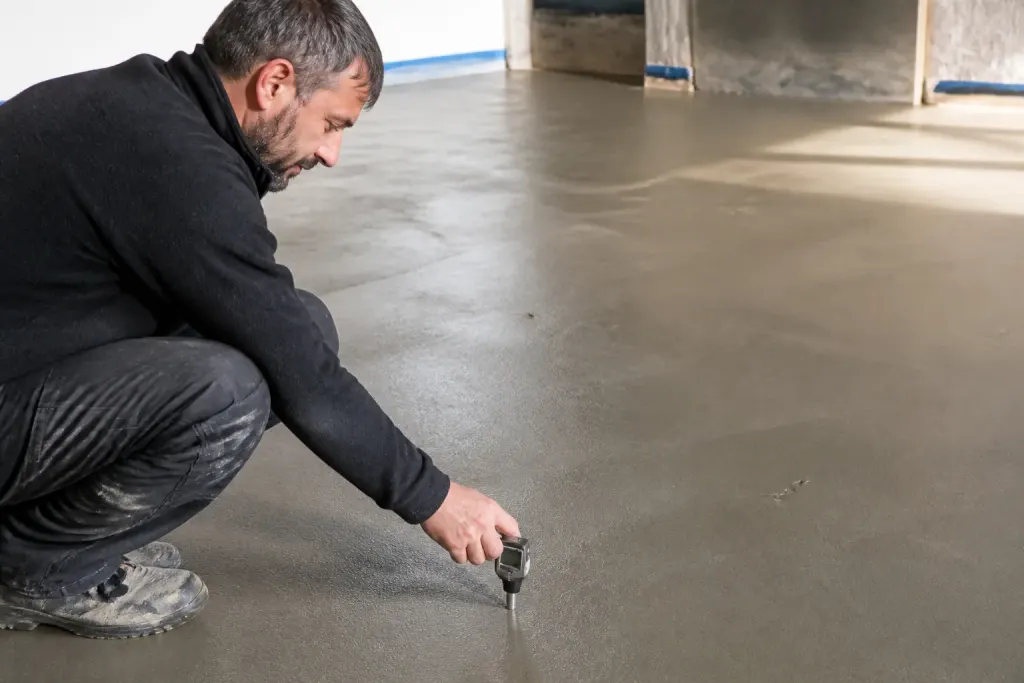 Ouvrier vérifiant une chape béton avec thermomètre numérique